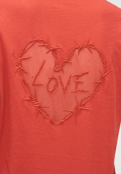 Κόκκινο βαμβακερό μπλουζάκι με σχέδιο καρδιάς από δίχτυ και κεντήματα. Η λέξη «LOVE» είναι κεντημένη μέσα στην καρδιά, περιγραμμένη με κλωστή.