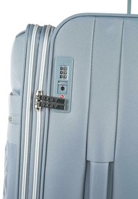 Maleta azul claro con textura acanalada, doble cremallera, candado TSA integrado y marca DKNY en los tiradores de las cremalleras. Presenta un asa lateral.