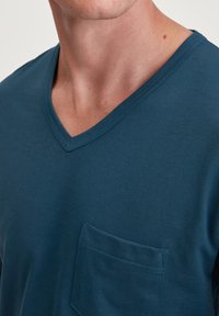 Teal v-hals t-shirt gemaakt van soepel katoen, met een borstzak en fijne ribstructuur langs de halslijn.