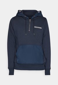 Hoodie navy con zip frontale, tessuto a trama e pannello inferiore liscio. Presenta una tasca frontale e un logo sul petto.