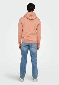 Ljusrosa hoodie tillverkad av mjukt tyg, med huva och ribbade ärmslut. Matchas med ljusblå jeans och vita sneakers.
