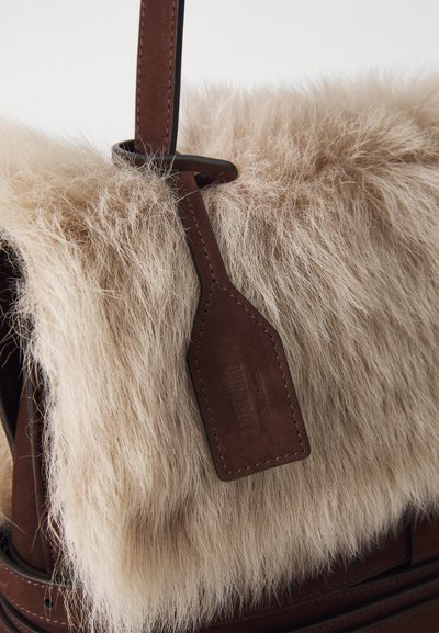 Sac à main en cuir marron avec un rabat en fausse fourrure douce couleur crème, texture lisse et une étiquette en cuir marron attachée.