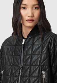 Gequiltede zwarte leren bomberjack met een gestructureerd ruitenpatroon, zilveren ritsen en een zwarte geribbelde kraag. Beschikt over ritszakken.