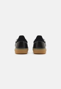 Black leather and suede sneakers with gum rubber soles, featuring a sleek design and minimalistic detailing on the back.