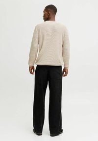 Pull en maille texturée beige clair avec un col rond, associé à un pantalon noir ample avec une poche arrière.