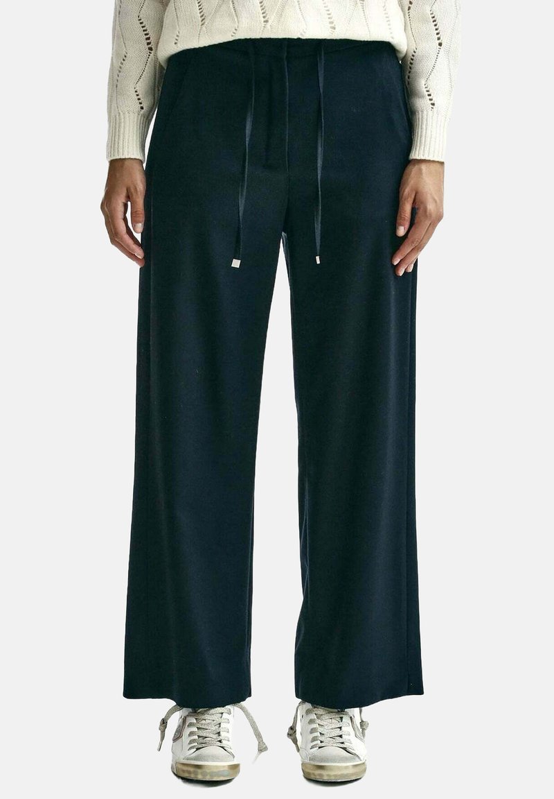 Pantaloni navy a gamba larga realizzati in tessuto morbido, con vita regolabile tramite cordoncino e inserti metallici, caratterizzati da una texture liscia. Abbinate a sneaker chiare.