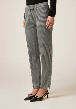 Zwart-witte houndstooth patroon broek met een getailleerde pasvorm, een gladde textuur en zijsplitsingen, gecombineerd met puntige zwarte hakken.