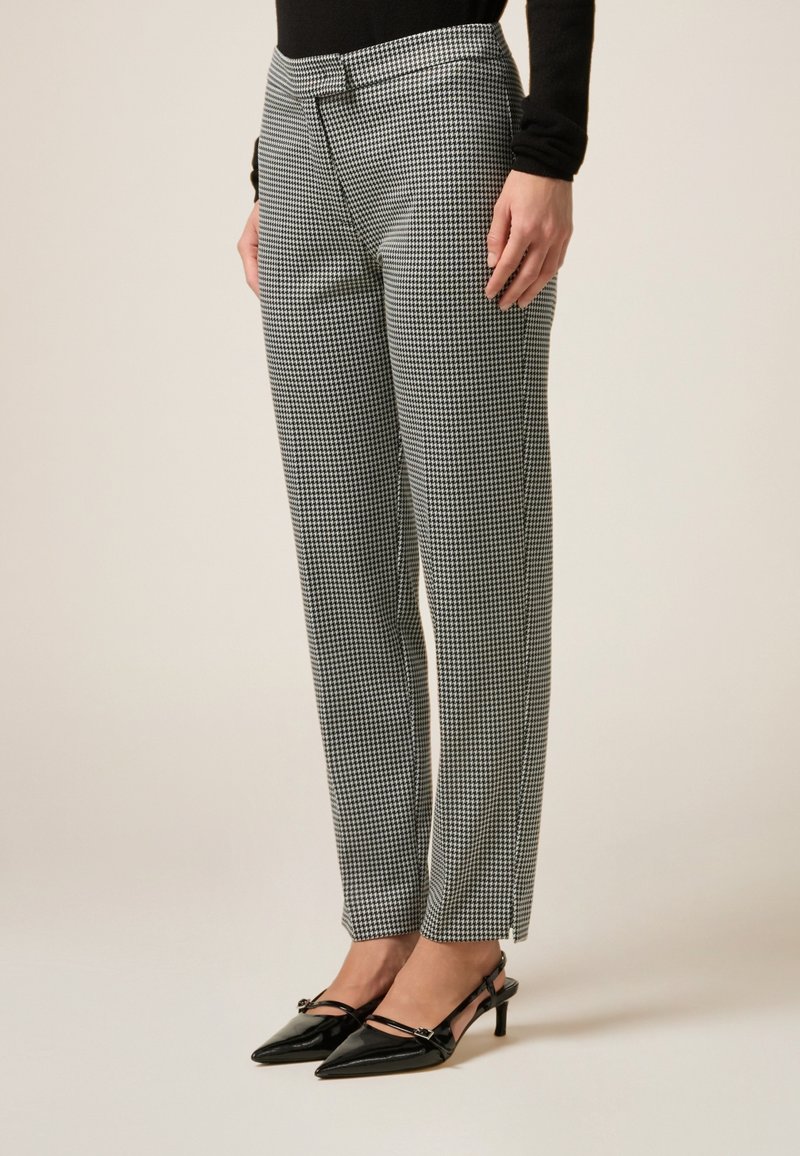 Zwart-witte houndstooth patroon broek met een getailleerde pasvorm, een gladde textuur en zijsplitsingen, gecombineerd met puntige zwarte hakken.