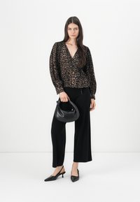 Smeđa bluzica s leopard uzorkom, s v-izrezom i napuhanim rukavima, u kombinaciji s crnim hlačama širokih nogavica. Dodatna oprema uključuje malu crnu torbicu i crne štikle.