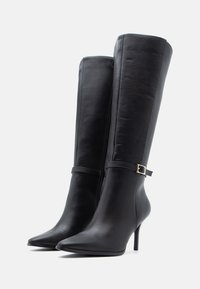Μαύρες δερμάτινες μπότες μέχρι το γόνατο με μυτερές μύτες, τακούνια στιλέτο, πλαϊκό φερμουάρ και λουράκι με χρυσό κούμπωμα. Λείος υφή.