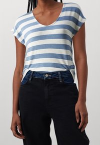 Striped t-shirt in light blue and white, featuring a v-neck and short sleeves, paired with high-waisted dark jeans with a button closure.