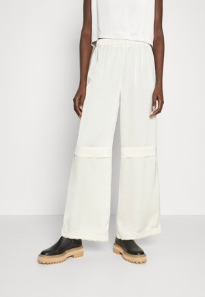 Flowy cream wide-leg trousers featuring a satin finish, elastic waistband, and contrast accents at the hem, paired with black chunky boots.