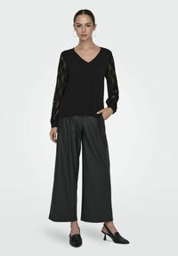 Czarna bluzka z dekoltem w serek i długimi rękawami z koronki, zestawiona z szerokimi czarnymi spodniami z ekoskóry i czarnymi bucikami na obcasie. Minimalistyczny design.