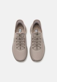 Light beige athletic shoes with a mesh upper, featuring a textured pattern, elastic laces, and a cushioned sole. Brand logo visible on the side.