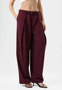 Burgundy wide-leg trousers with pleats and a buckle detail at the waist. Made of a smooth fabric, featuring side pockets and a loose fit.