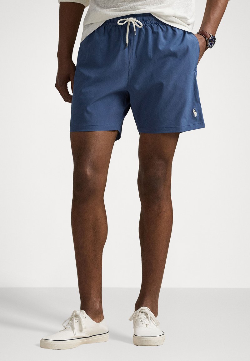 Blue swim shorts made of lightweight fabric, featuring an elastic waistband with a drawstring and a small logo detail.