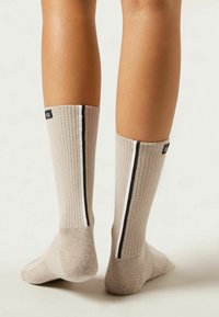 Beige rillede sokker med mørke og lyse side-striber. Har et sort label øverst. Materialet ser blødt og strækbart ud.