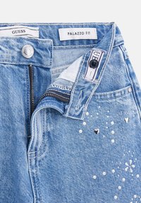 Light blue denim palazzo fit jeans with a zipper, silver button closure, and decorative studs, including hearts and flowers, on the front.