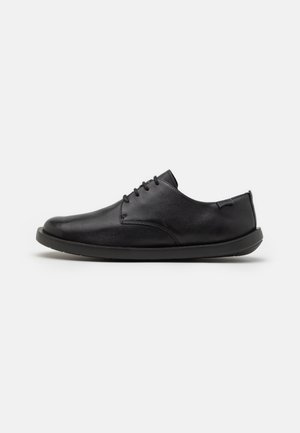 Chaussure habillée en cuir noir à lacets, bout rond et semelle plate, vue de profil sur fond blanc.