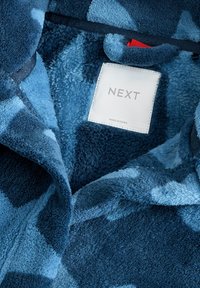Blaue Fleece-Bekleidung mit weicher Textur, abstraktem Muster und einem Etikett mit "NEXT." Enthält einen Reißverschluss-Detail an der Vorderseite.