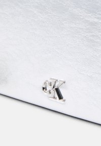 Sudraba mākslīgās ādas rokassoma ar teksturētu virsmu un metāliski CK logotipa akcentu. Kompakts dizains ar elegantu, minimālistisku stilu.