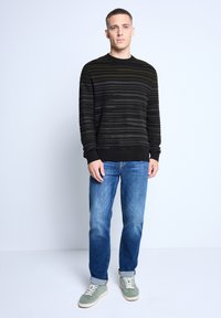 Black and green striped knit sweater with a round neckline, paired with blue jeans and green sneakers. Casual fit, ribbed cuffs and hem.