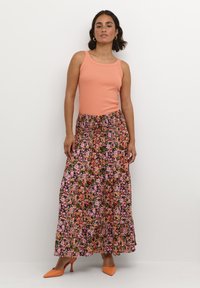 Un débardeur pêche associé à une longue jupe fleurie ornée de fleurs roses et oranges sur un fond noir. Des talons aiguilles orange viennent parfaire le look.