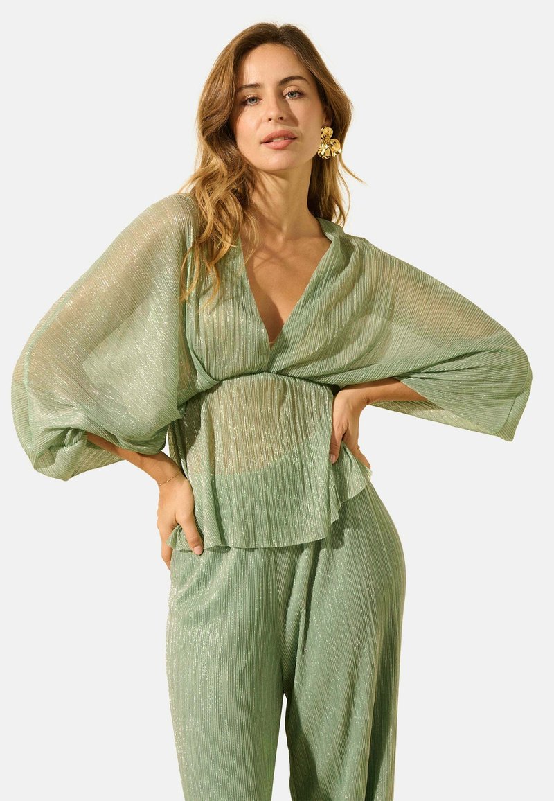 Haut plissé léger vert clair, transparent, avec des manches larges et un décolleté en V profond, associé à un pantalon plissé assorti. Texture brillante notable sur l'ensemble.