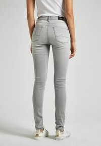 Jeans ajustados de color gris hechos de mezclilla, con dos bolsillos traseros con costuras en forma de ola y una cintura de altura media. Combinados con zapatillas blancas.