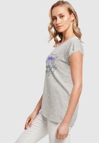 Graues T-Shirt mit kurzen Ärmeln und lockerer Passform, mit einem lila Libellen-Graphic und geschwungener Schrift. Weicher Stoff mit glatter Textur.