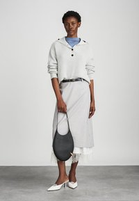 Pull en maille côtelée gris clair avec capuche, superposé à un haut bleu. Jupe grise avec bord en dentelle et sac à épaule noir. Talons blancs.