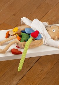 Child-sized anatomical doll with removable soft organs, including a red heart and green intestines, lying on a white table on a wooden floor.