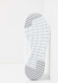 Sula av en vit Skechers-sko med strukturerat mönster och grå gummisektioner på hälen och tån för bättre grepp.