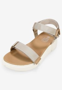 Sandalia de tiras beige con tiras elásticas anchas, plantilla marrón y suela blanca. Presenta hebillas ajustables y acentos de tela texturizada.