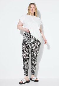 Witte T-shirt met korte mouwen, gecombineerd met zwart-witte legging met luipaardprint. Model draagt zwarte sandalen met witte accenten. Zachte texturen overal.