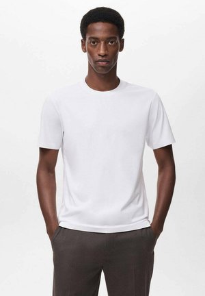 Camiseta blanca de algodón de manga corta con escote redondo, textura suave y un corte regular, combinada con pantalones oscuros y ajustados.