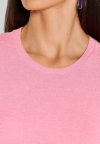 Rosa gerippter Pullover mit rundem Ausschnitt. Weiche Textur, mit dezenten horizontalen Linien. Nahaufnahme, keine weiteren Details.