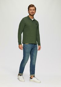 Groene polo met lange mouwen en een kraag, voorzien van een klein logo. Combinatie met lichtblauwe jeans en witte sneakers, casual gestyled.