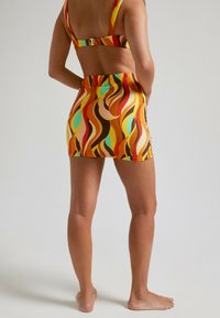 Conjunto de baño con un patrón espiral multicolor en naranja, marrón y teal. El material es suave con un diseño ajustado y tirantes ajustables.