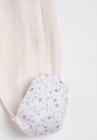 Tissu côtelé rose clair avec un patch ovale blanc présentant un petit motif floral rose et vert cousu dessus.