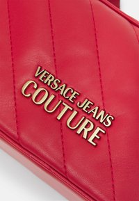 Borsa rossa in pelle con texture trapuntata, con il logo dorato "VERSACE JEANS COUTURE" ben in evidenza.