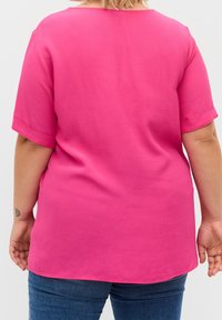 Top fucsia a maniche corte con scollo arrotondato e vestibilità relax. Tessuto morbido e liscio; la parte posteriore presenta un orlo leggermente curvo.