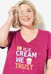 T-shirt a V in fucsia con maniche corte. Presenta un testo colorato "IN ICE CREAM WE TRUST" e grafiche di gelato. Tessuto morbido.