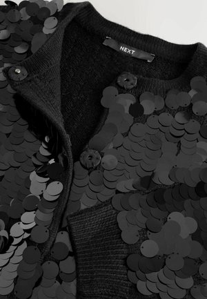 Black cardigan featuring a textured knit and large black sequins. Two buttons at the neck and a smooth fabric interior are visible.
