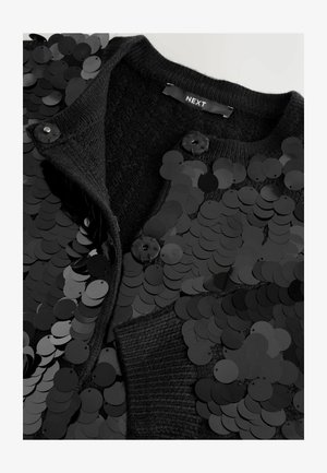 Black cardigan featuring a textured knit and large black sequins. Two buttons at the neck and a smooth fabric interior are visible.