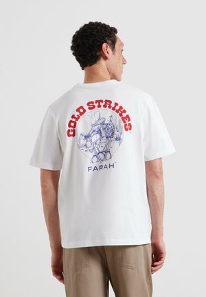 Uomo che indossa una maglietta bianca con un "COLD STRIKES" rosso e un disegno di cactus blu e testo "FARAH" sul retro.