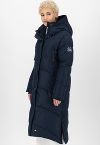 Giacca puffer blu navy, design lungo con cappuccio, chiusura frontale con zip, tasche anteriori, texture trapuntata e patch con logo sulla manica.