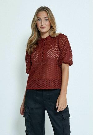 Roestkleurige, textuur blouse met chevronpatroon, ronde halslijn en knoopdetail. Korte puffmouwen; gecombineerd met zwarte, losse cargo-broek.