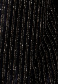 Tessuto nero con strisce verticali di filo dorato, creando un design testurizzato. Texture morbida con una leggera lucentezza data dagli accenti metallici.