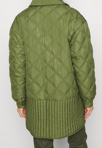 Abrigo acolchado en verde oliva con patrón de diamantes, bajo acanalado y detalle de botones en las mangas. Material suave y texturado.